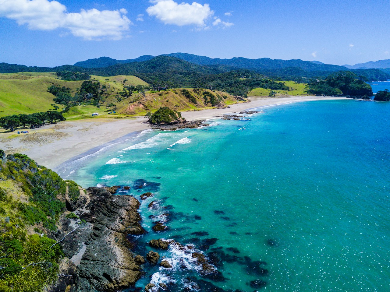 Turquoise New Zealand coastline and green hills in a boutique accommodation concept website.