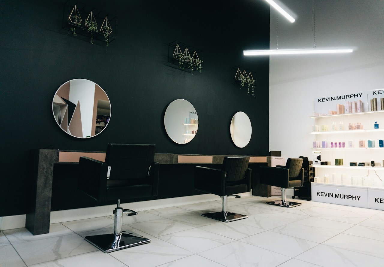 Elegant hair salon with dark walls, round mirrors and professional styling chairs.